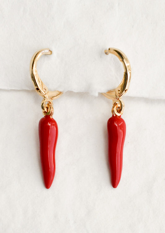 A pair of gold huggie hoop earrings with red pepper charm.