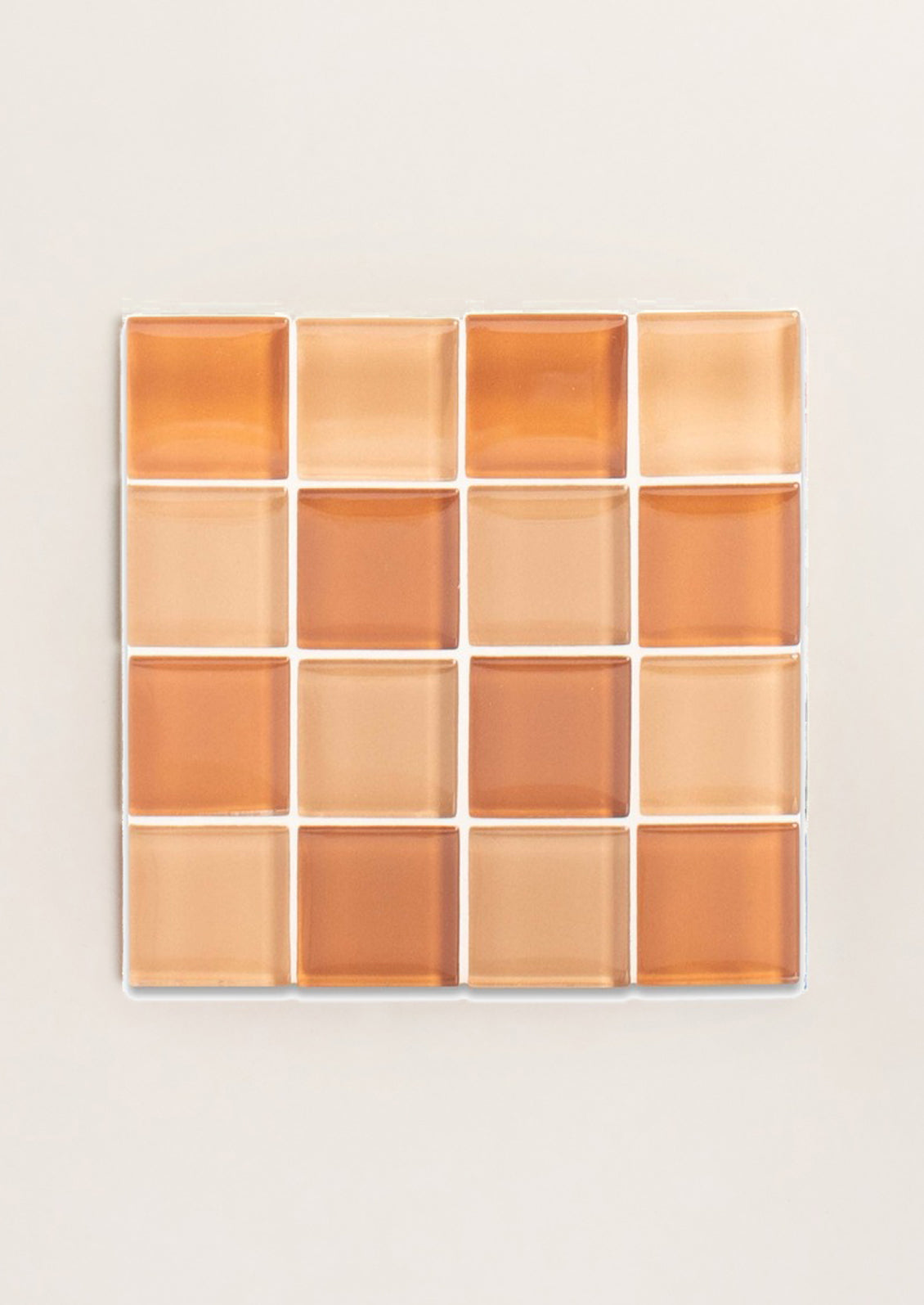 A glass tile coaster in two tone checker pattern in light peach and dark peach.