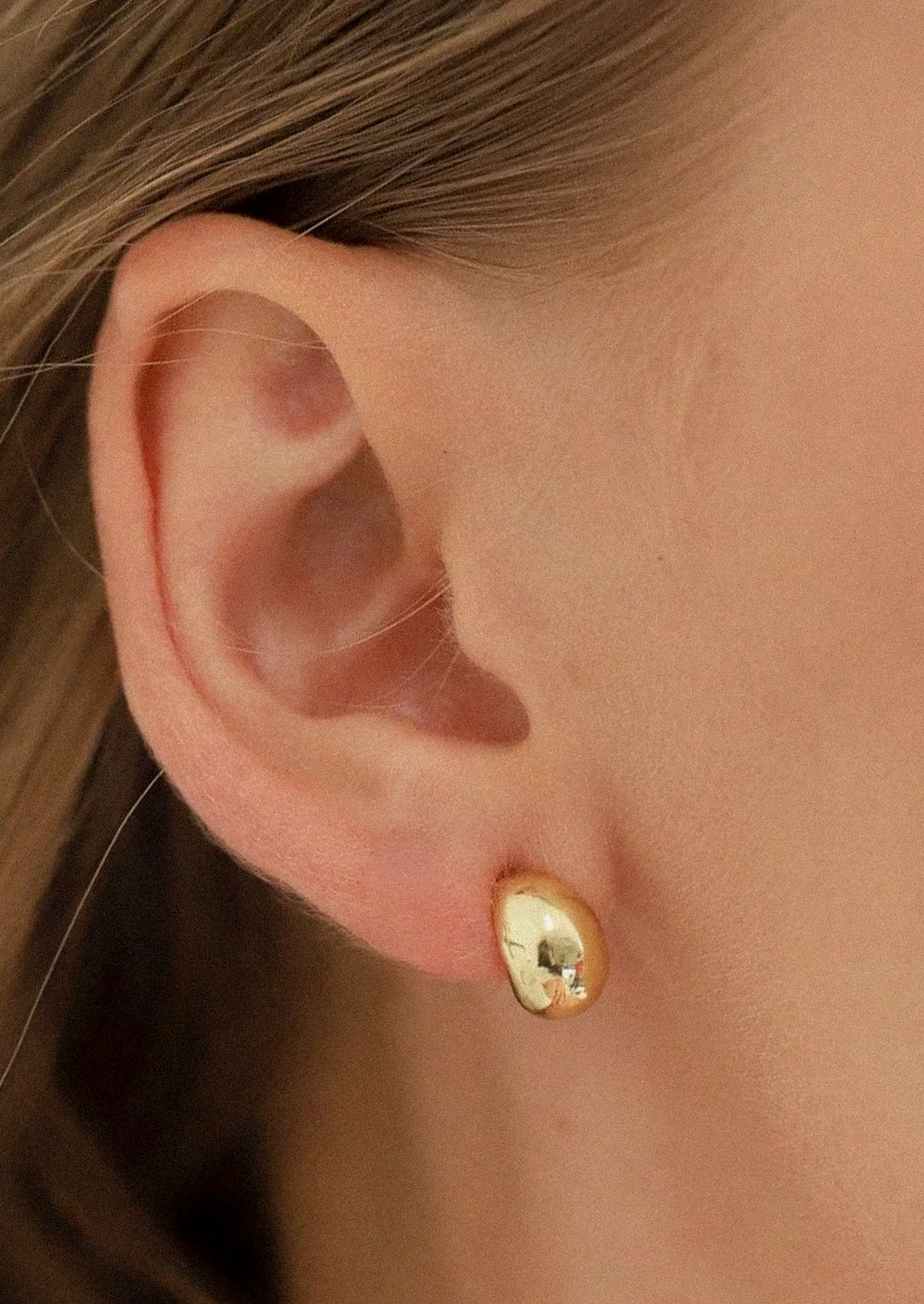 A woman wearing a gold teardrop shaped earring.