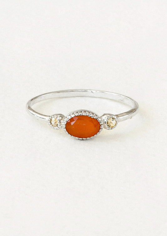A sterling silver ring with a carnelian oval in the center framed by two small round citrine stones on either side.