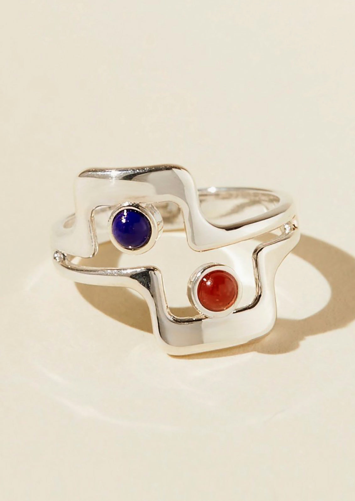 A silver geometric ring with blue and red glass cabochons at open middle.
