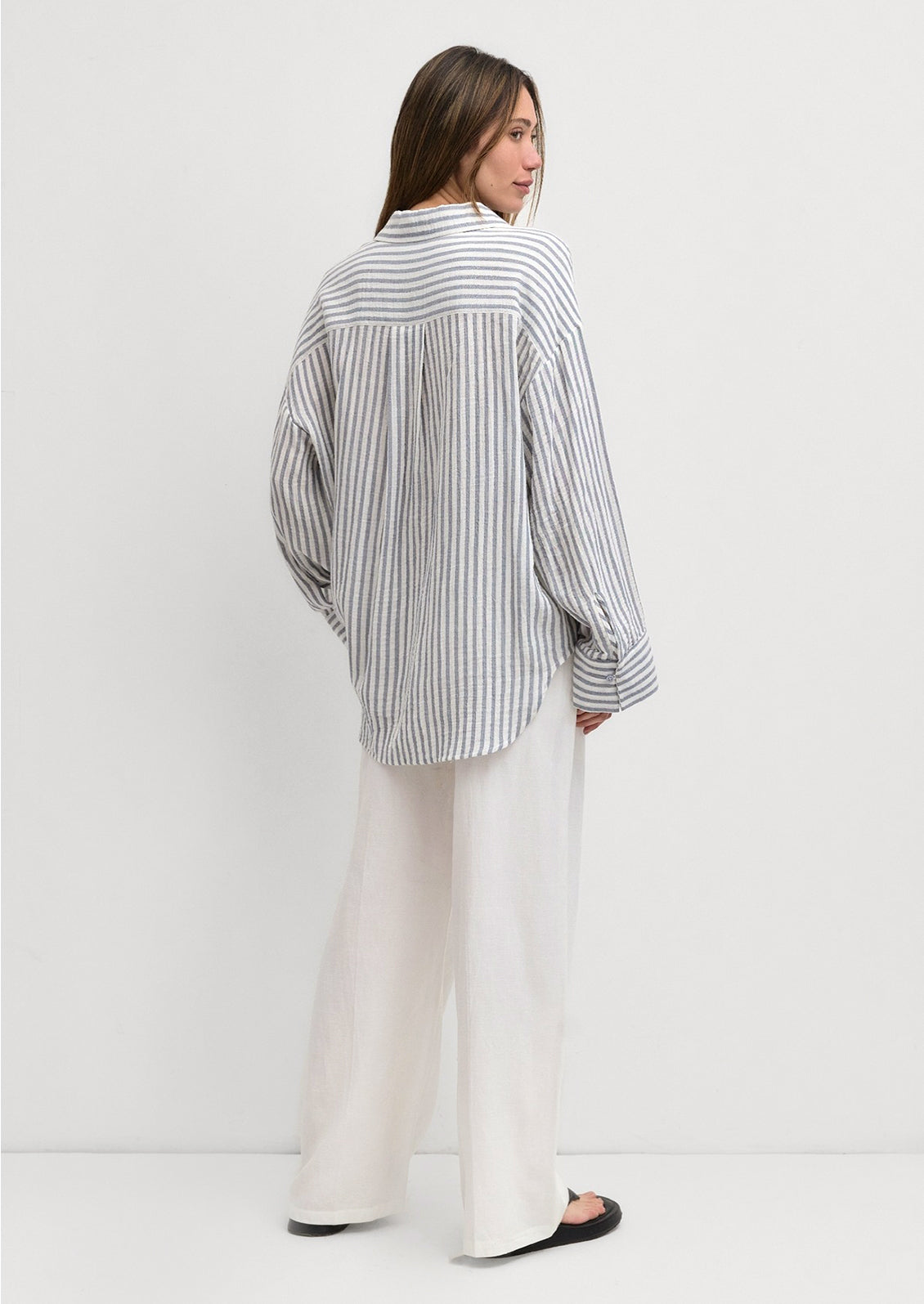 A woman wearing a white and blue stripe cotton gauze button down shirt.