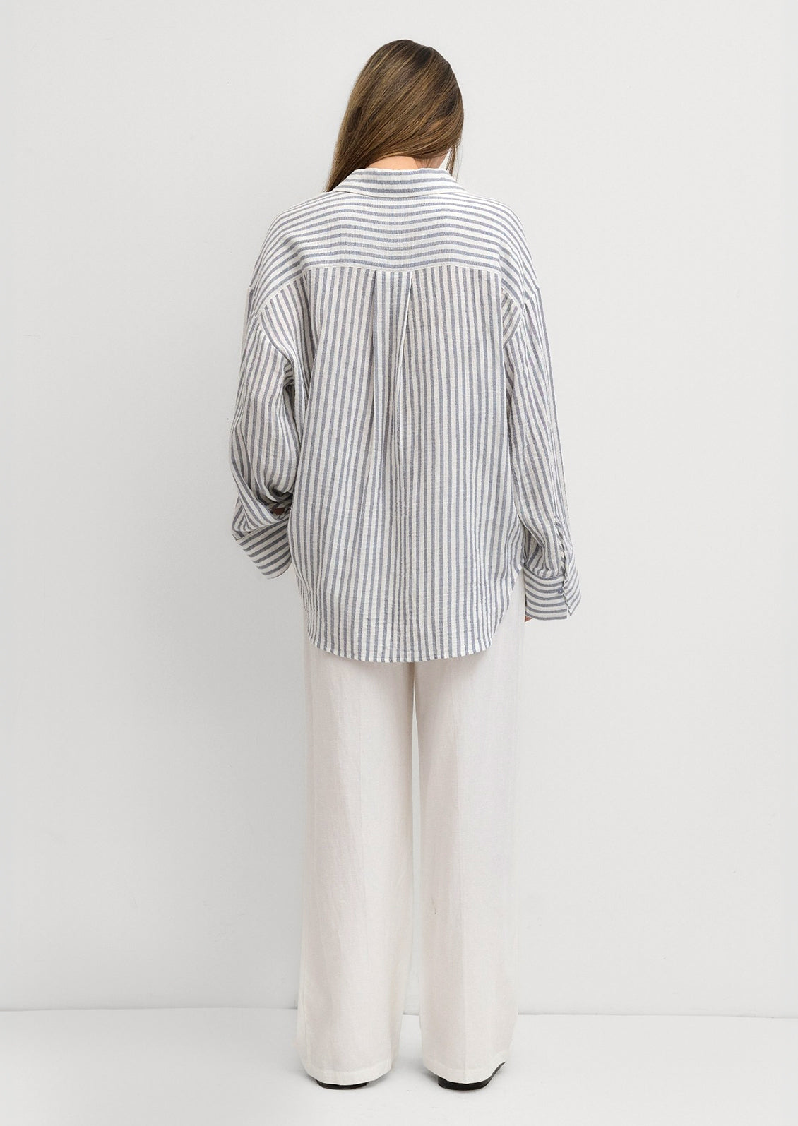 A woman wearing a white and blue stripe cotton gauze button down shirt.