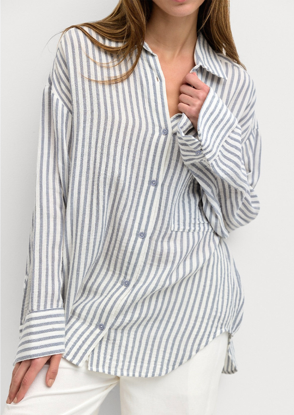 A woman wearing a white and blue stripe cotton gauze button down shirt.