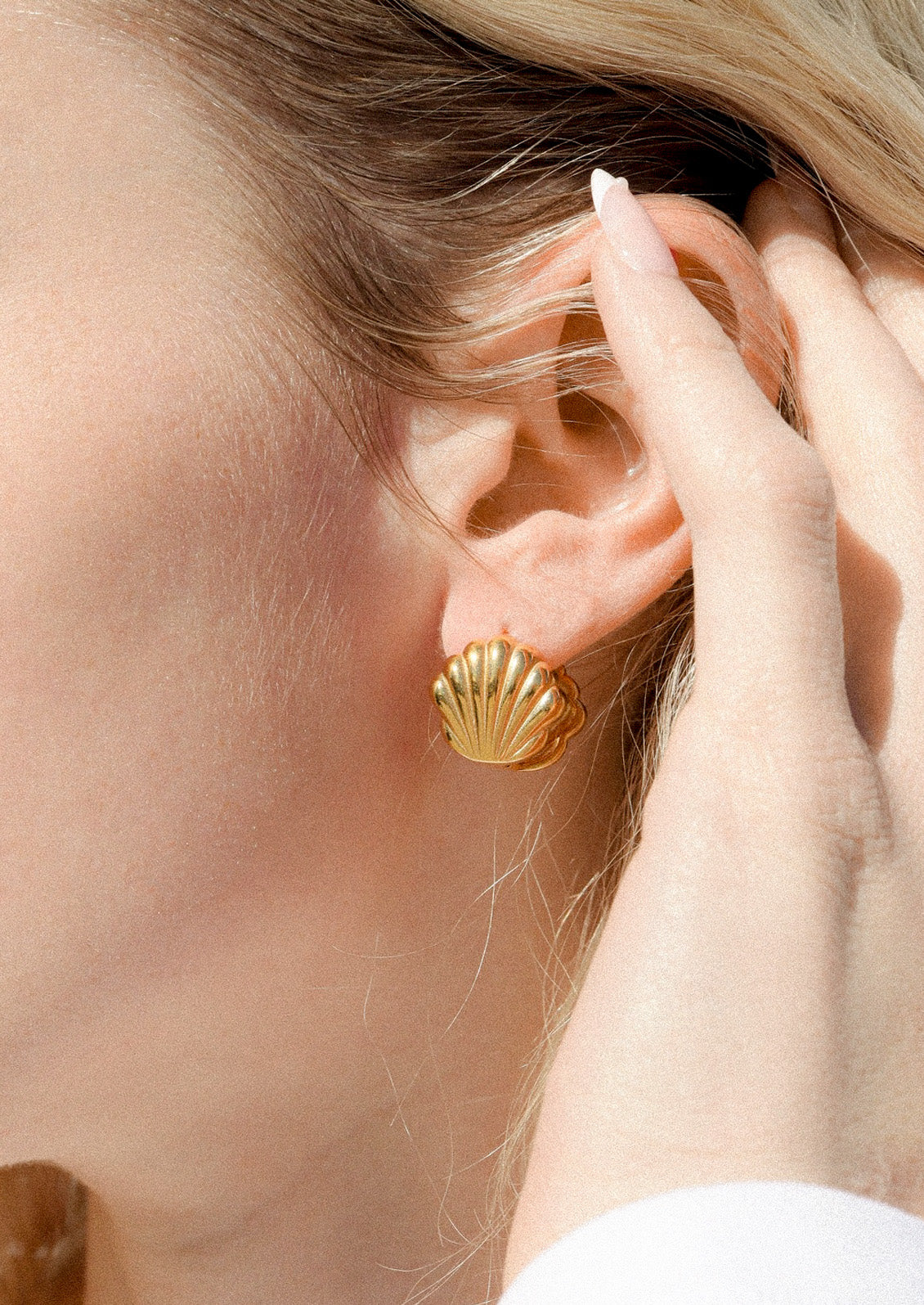 A woman wearing a gold earring in the shape of a concha shell.