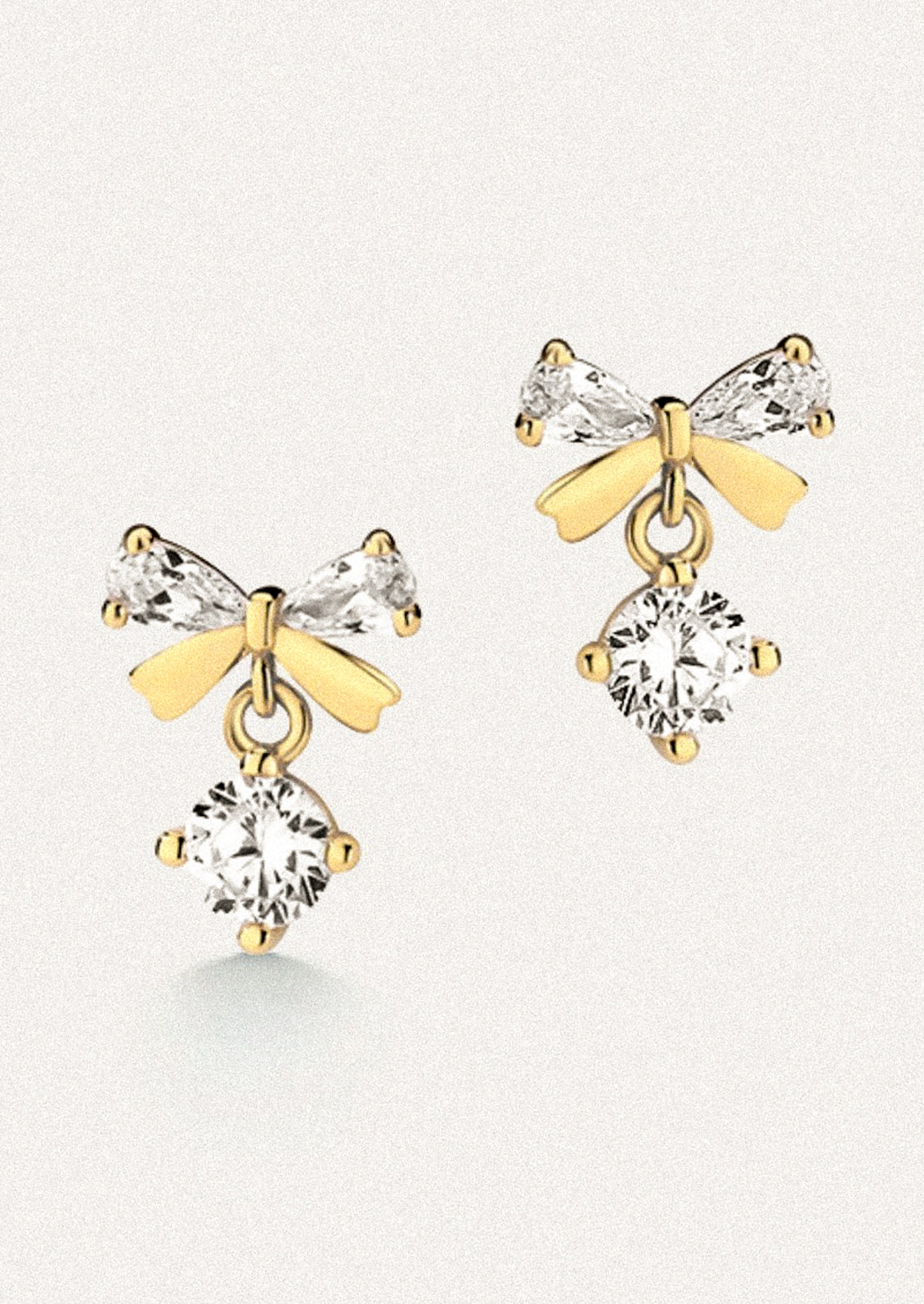 A pair of gold stud earrings in the shape of a bow with clear crystal accents.