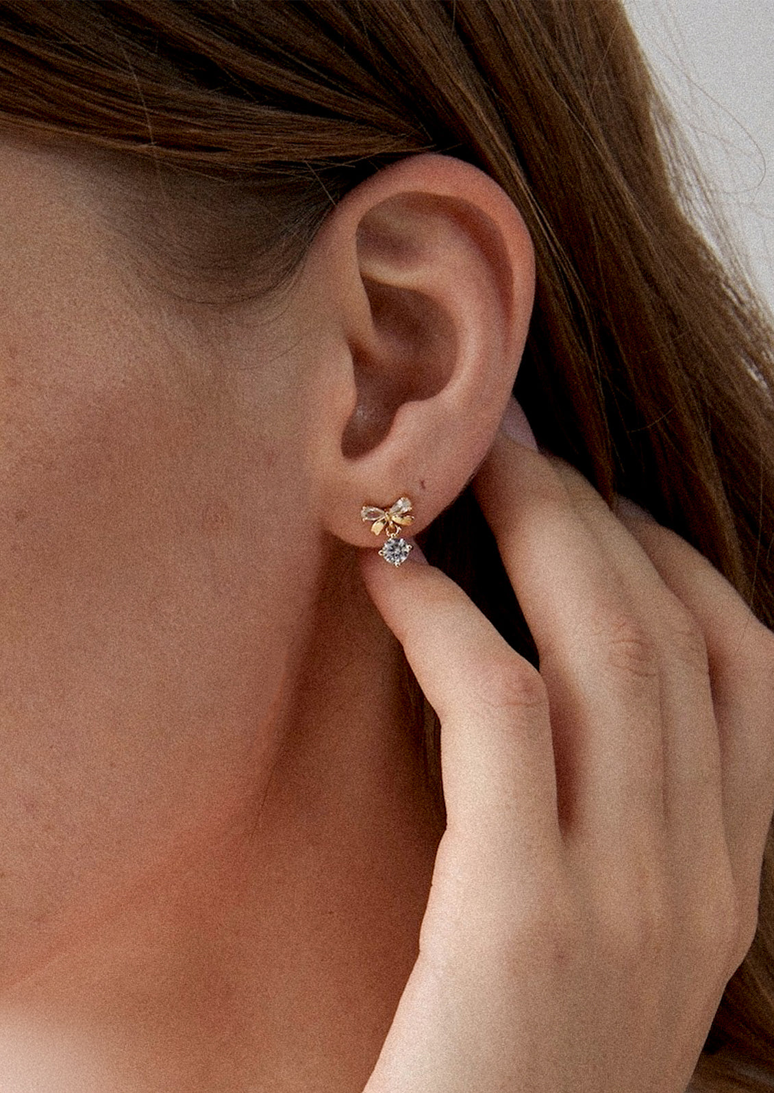A person wearing a pair of bow shaped studs with crystal accents.