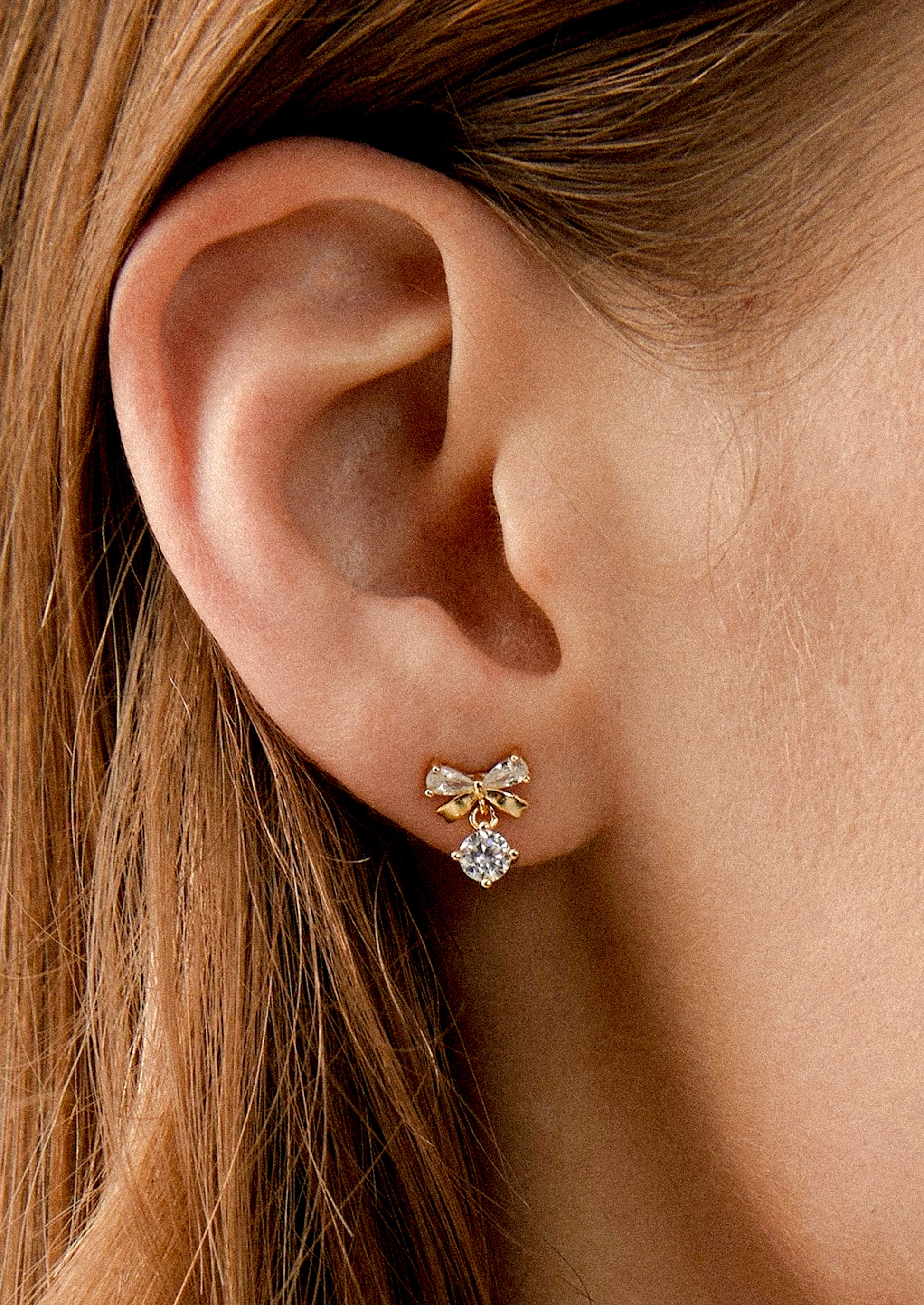A person wearing a pair of bow shaped studs with crystal accents.