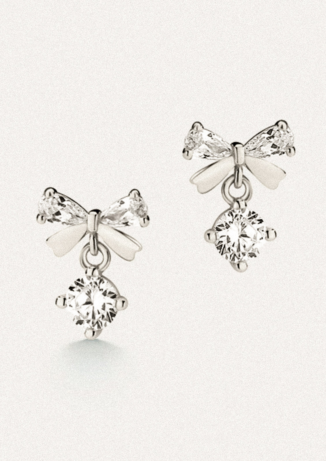 A pair of silver stud earrings in the shape of a bow with clear crystal accents.