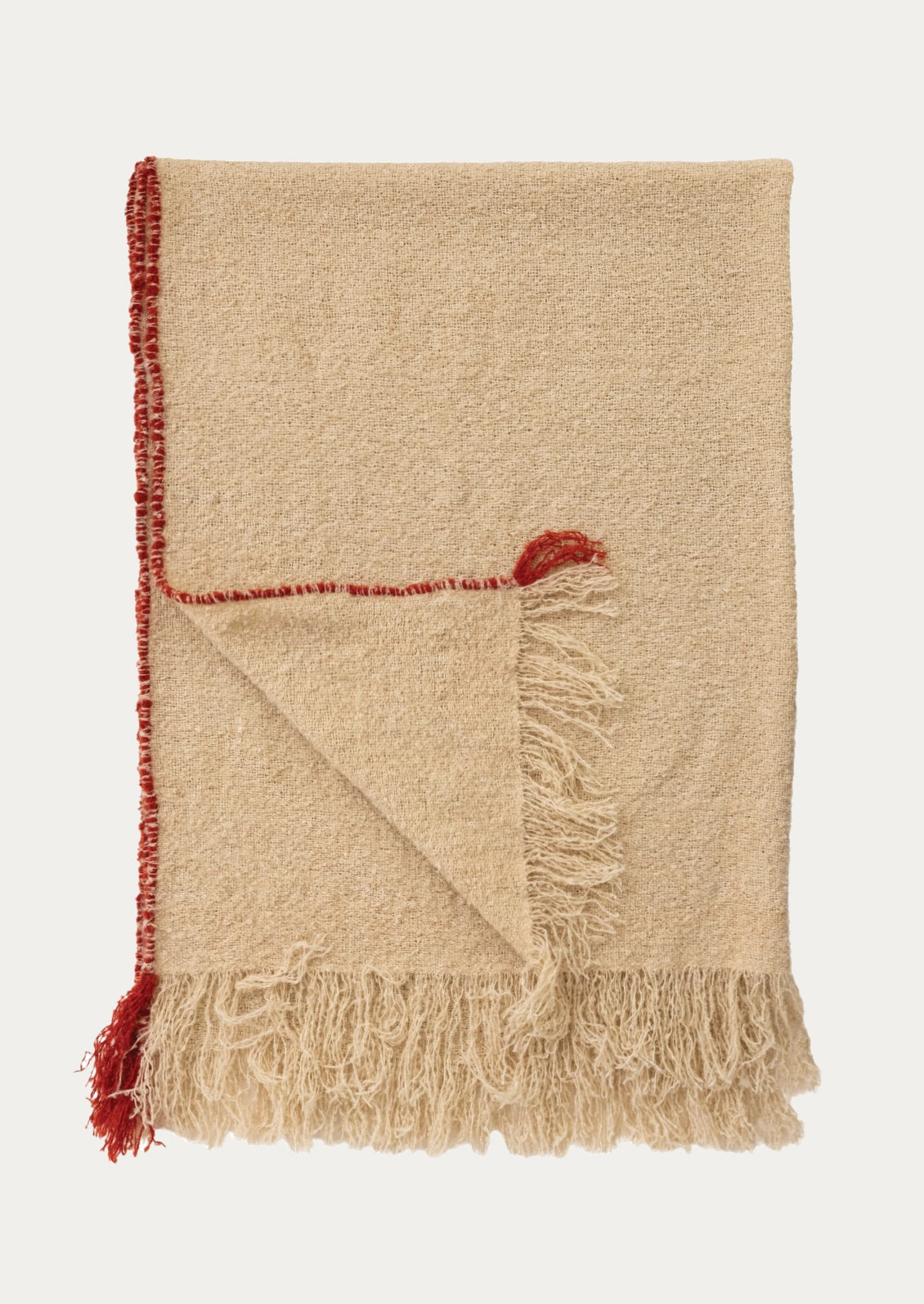 A folded beige woven throw blanket with fringed edges and a contrasting red tassel detail, shown on a light gray background.