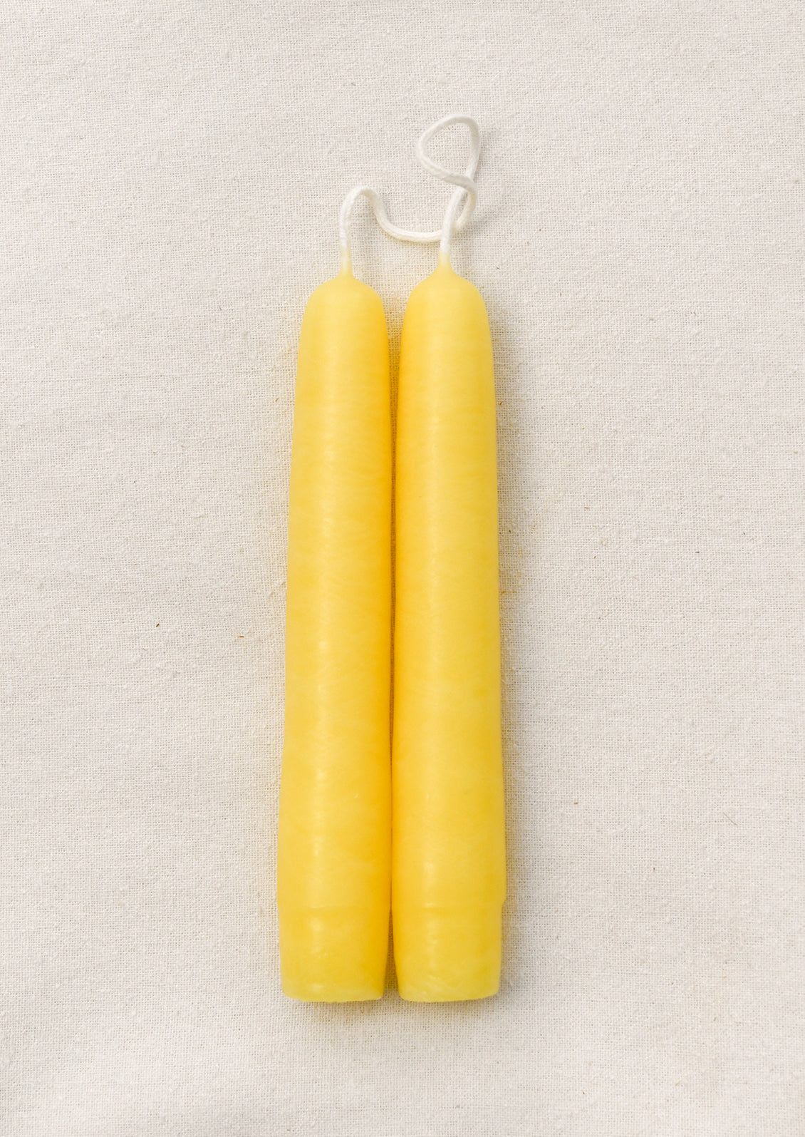 Two yellow candles with white wicks on a light beige background