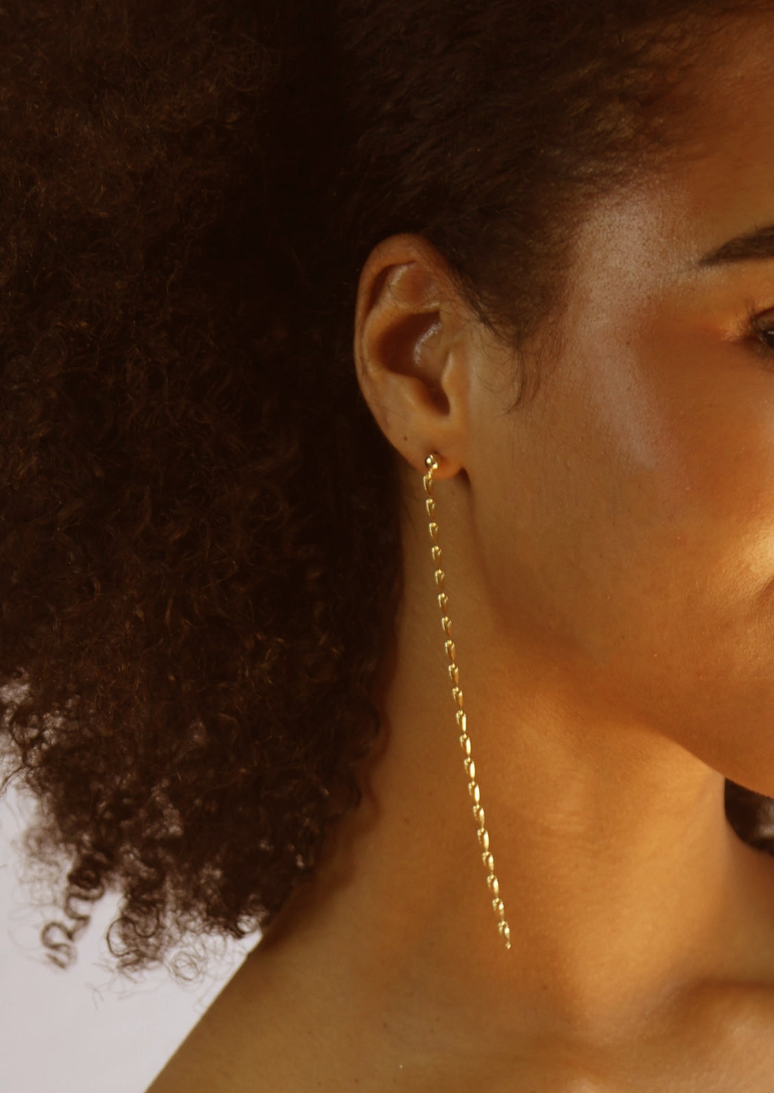 A pair of gold earrings with round ball post and long, dangling gold chain.