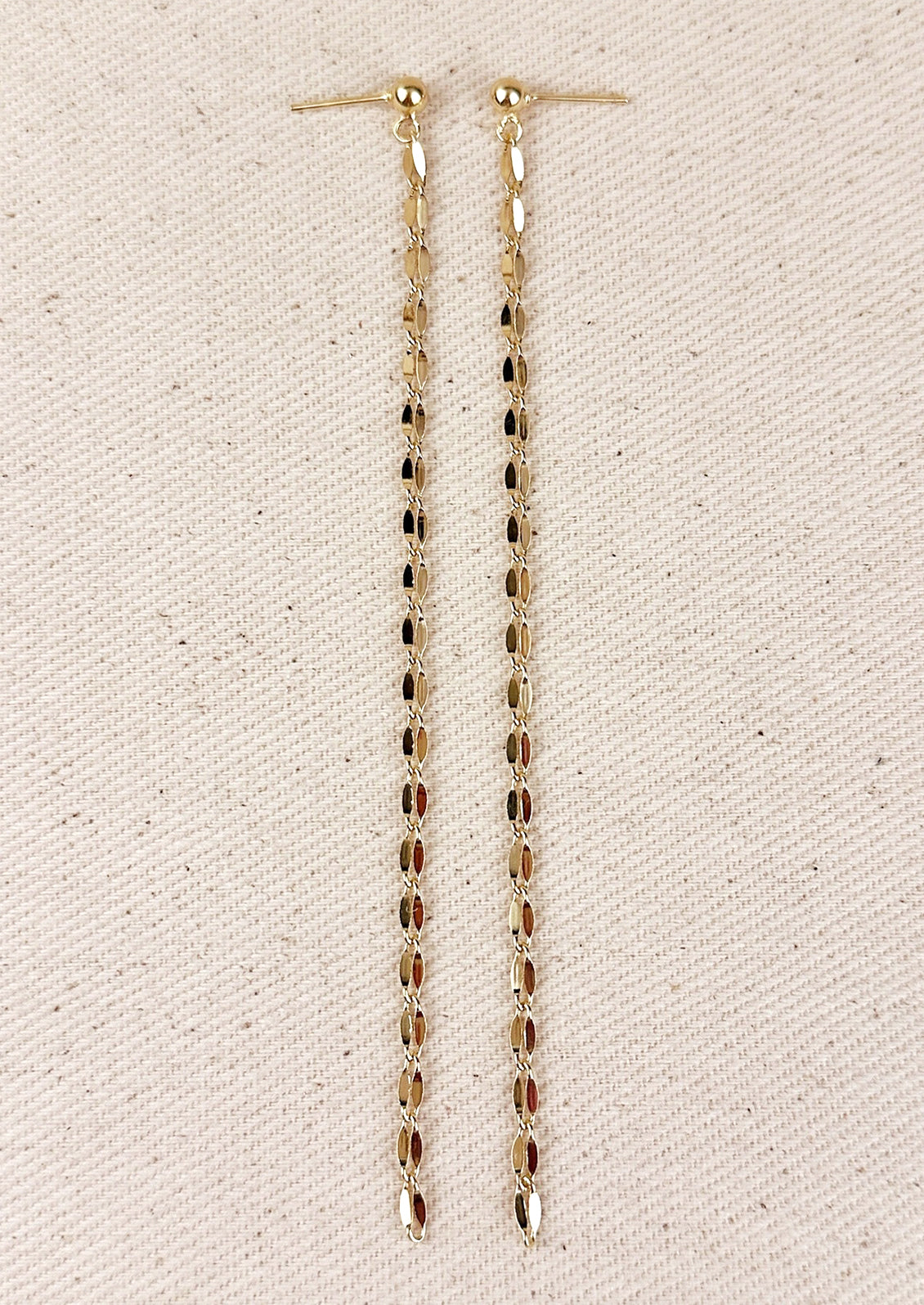 A pair of gold earrings with round ball post and long, dangling gold chain.
