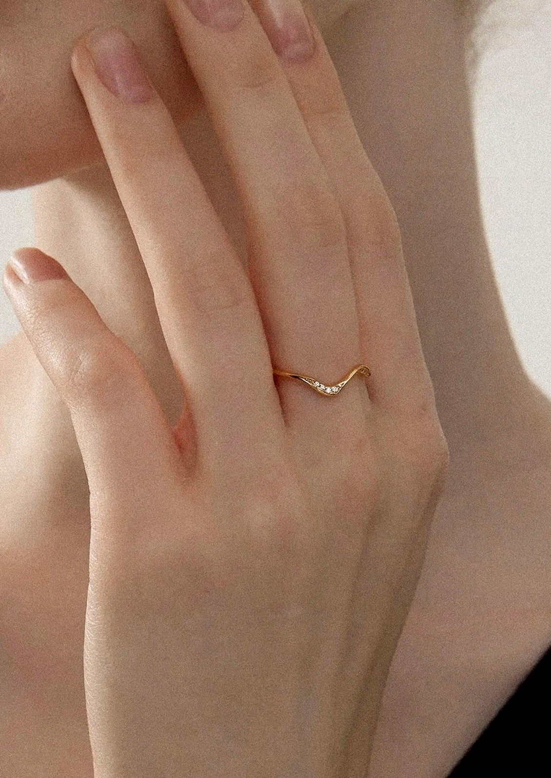 A person wearing a wavy gold ring with crystal detailing.