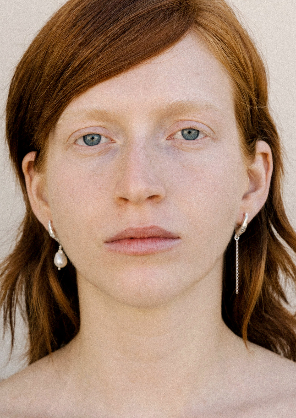 A woman wearing a pair of mismatched sterling silver earrings with a freshwater pearl.