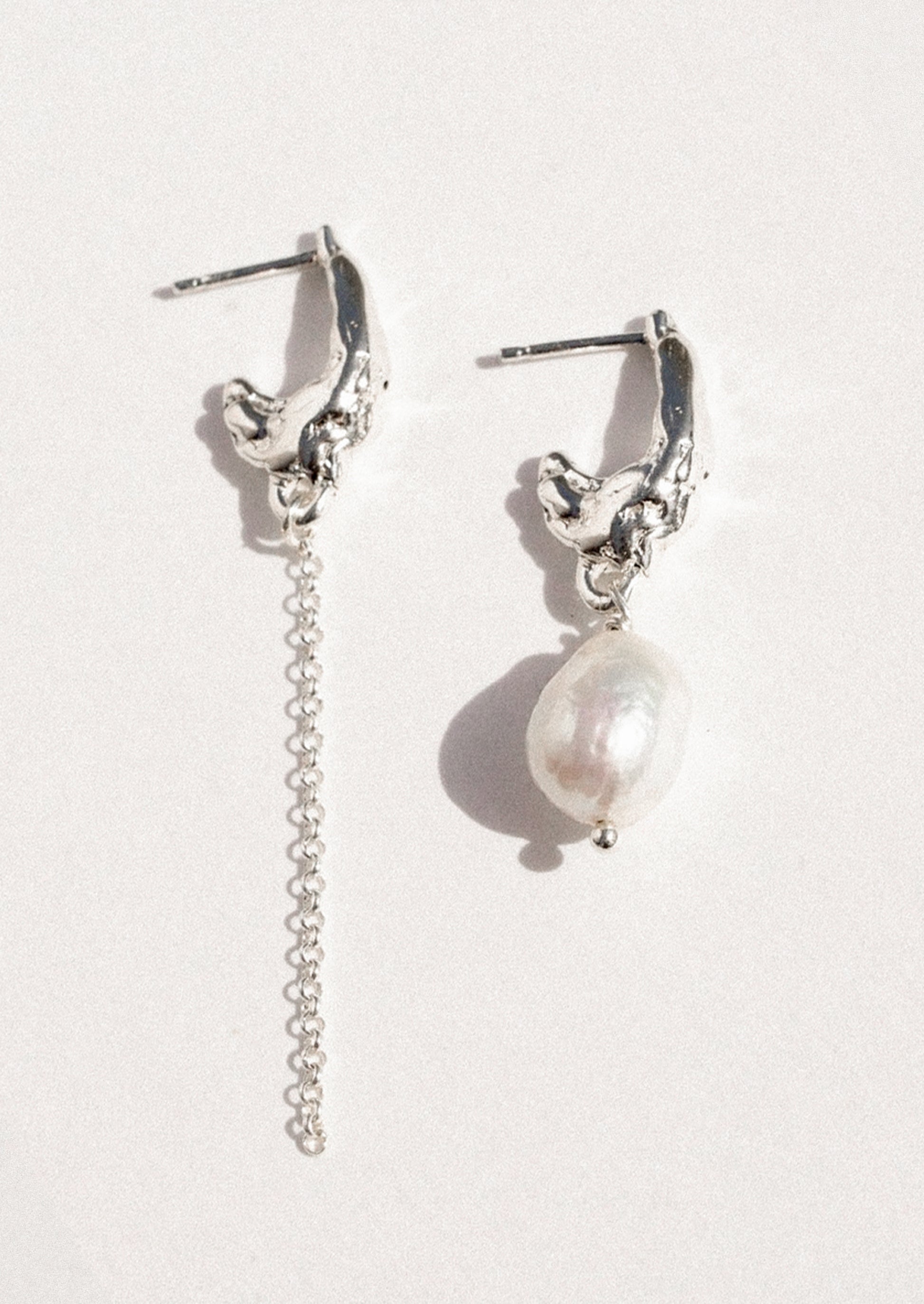 A pair of mismatched sterling silver earrings with a freshwater pearl.