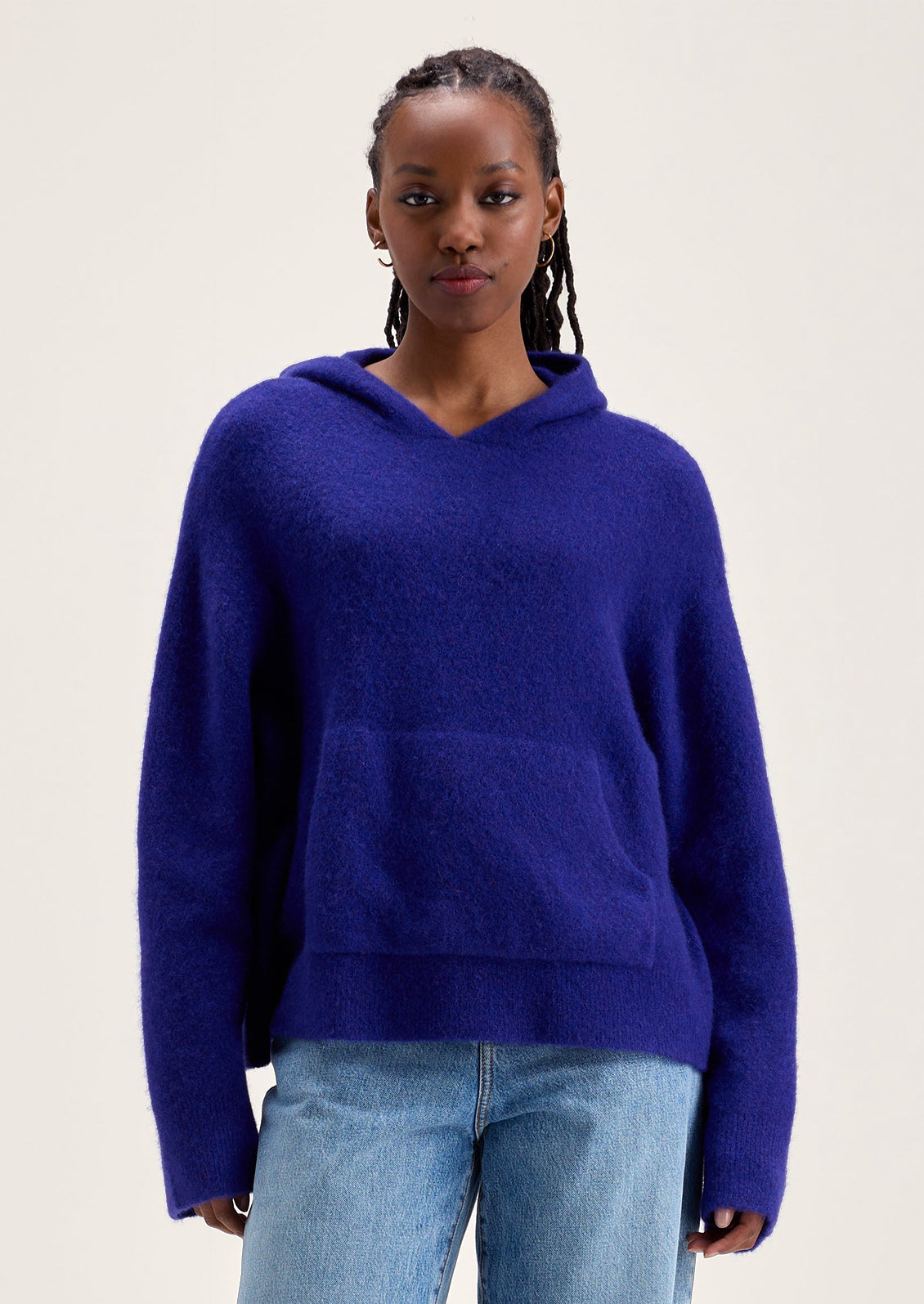 A woman wearing a hooded sweater with kangaroo pocket in vibrant cobalt blue color.