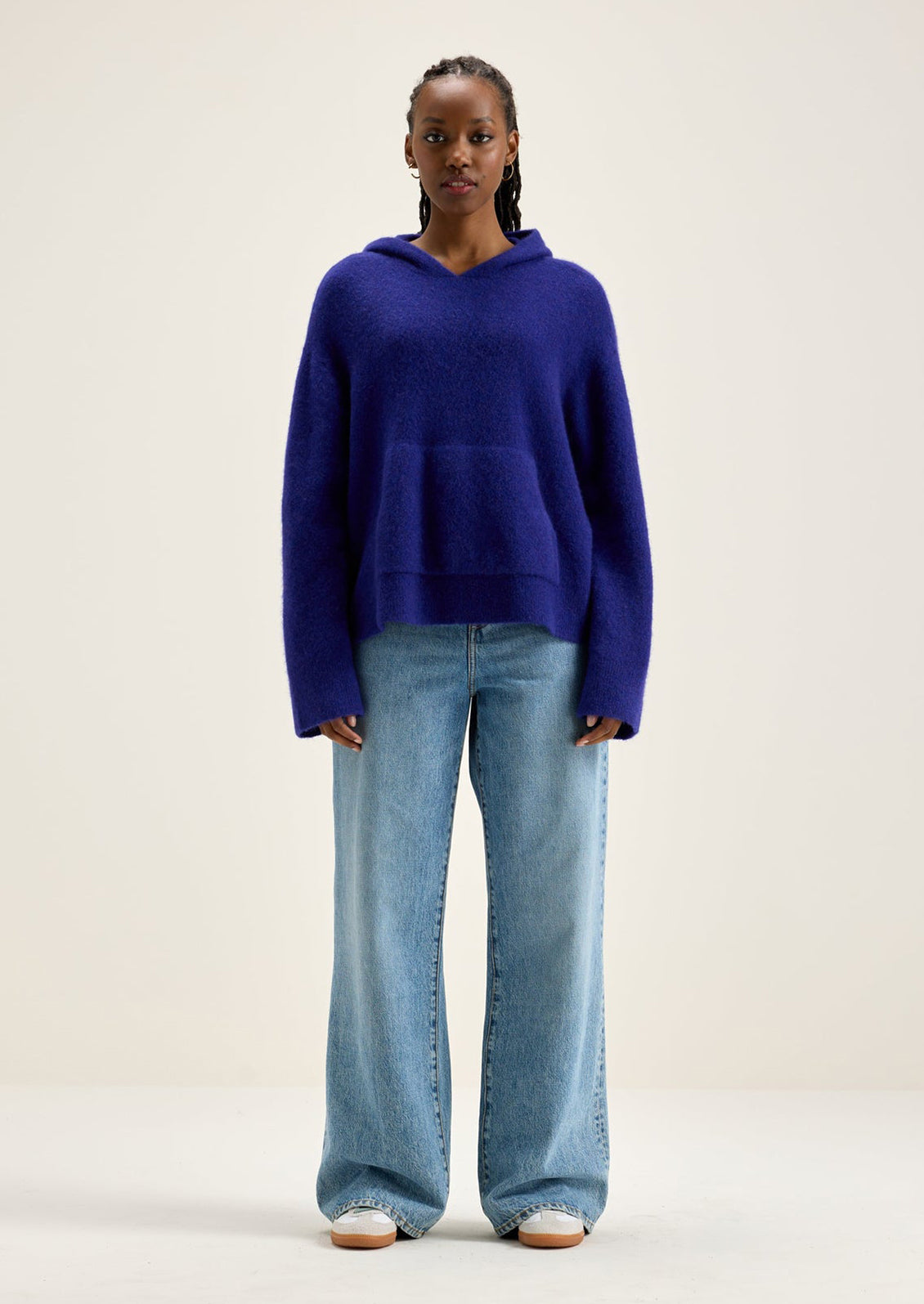 A woman wearing a hooded sweater with kangaroo pocket in vibrant cobalt blue color.