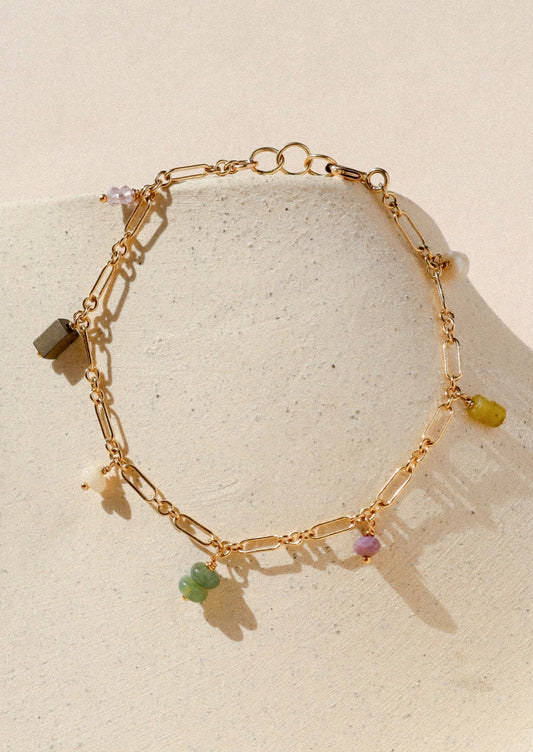 A gold chain bracelet with various colored gems.