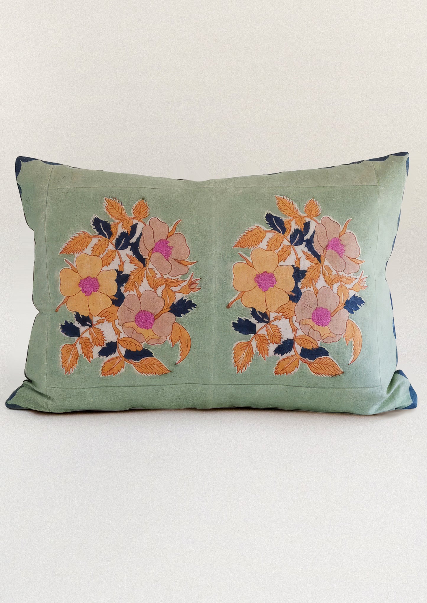 A block printed throw pillow in mint green with orange floral print.