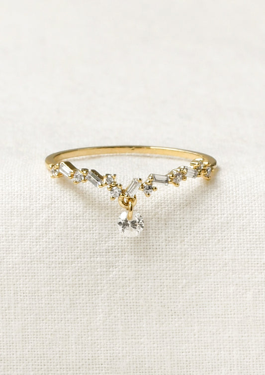 A gold ring with a dipped v design adorned with small variously shaped cubic zirconia and a large round one dangling from the center.