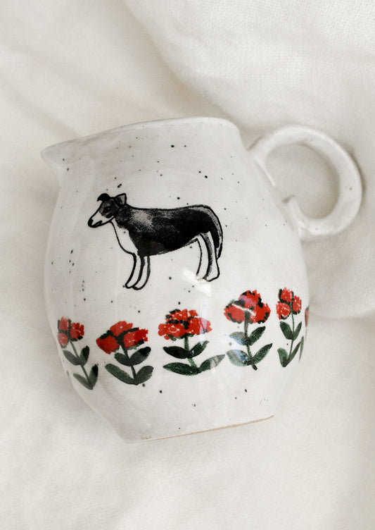 A small speckled white ceramic pitcher with illustration of dog with red flowers.