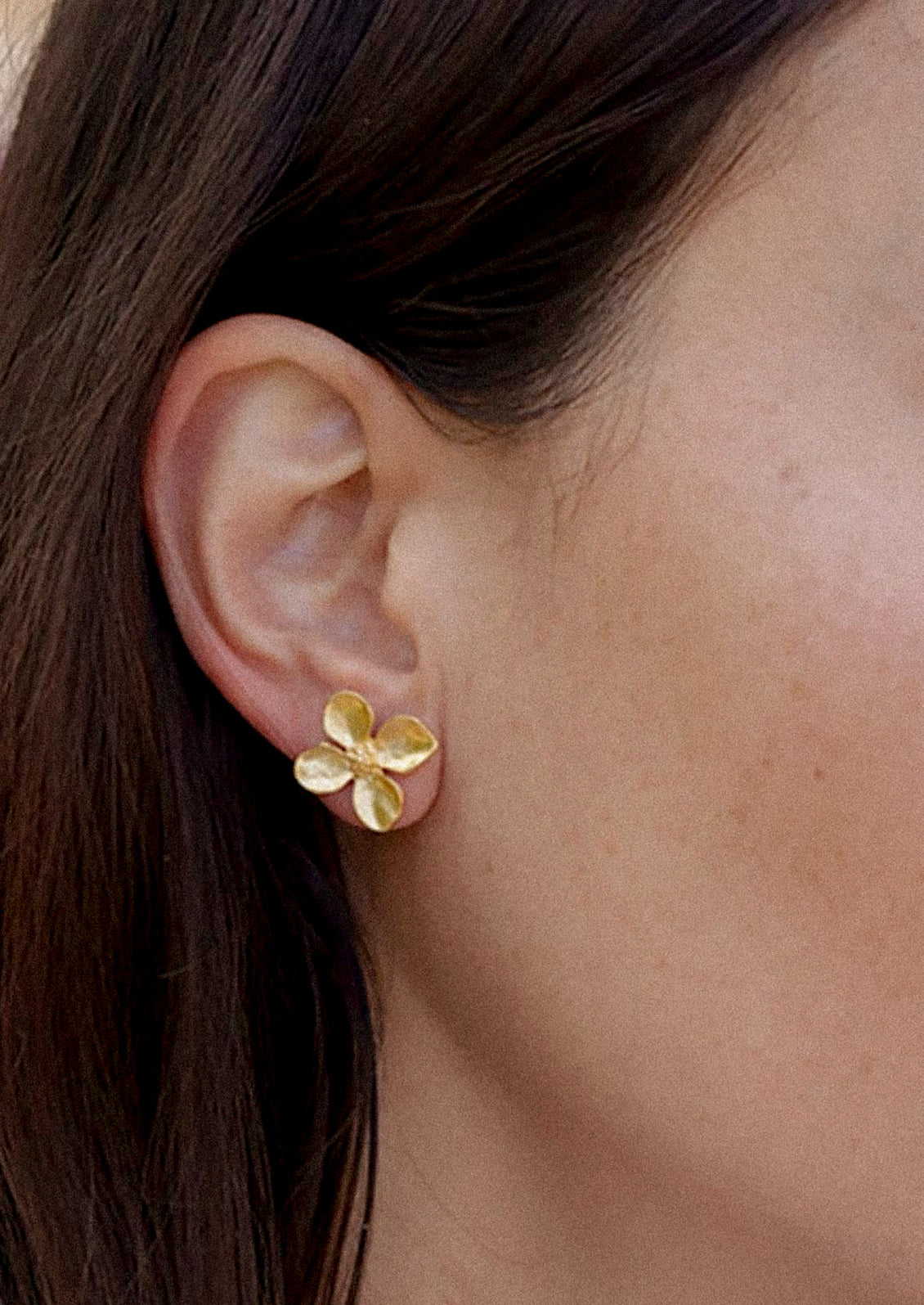 A pair of gold earrings in the shape of a flower with four petals.