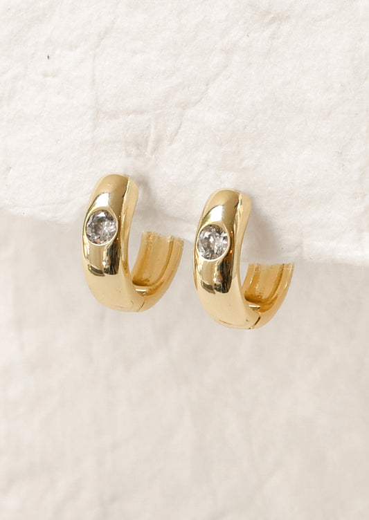 A pair of gold hoop earrings with a round diamond on the front.