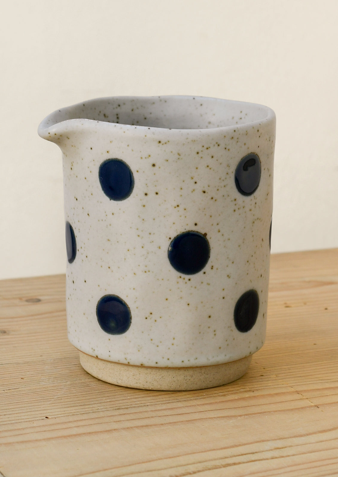 A speckled gray ceramic creamer with navy blue polka dots.