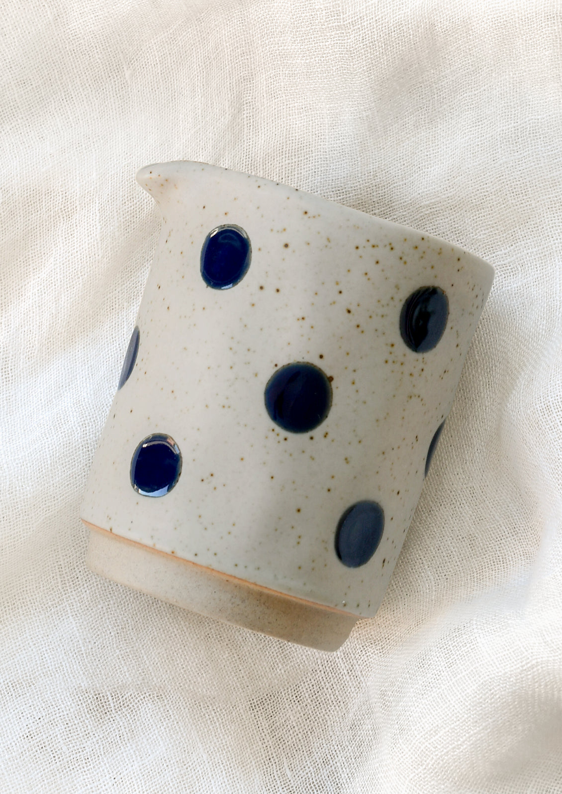 A speckled gray ceramic creamer with navy blue polka dots.
