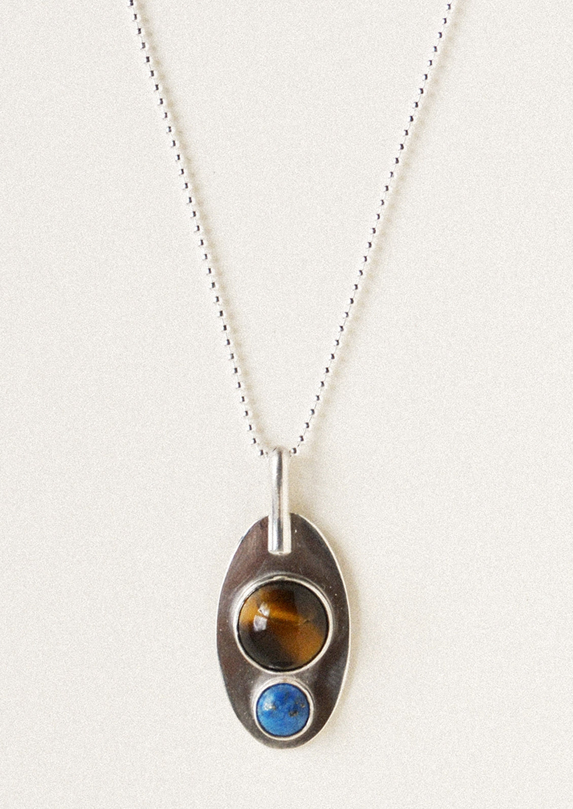 A silver necklace with pendant adorned with a brown gemstone and blue gemstone.