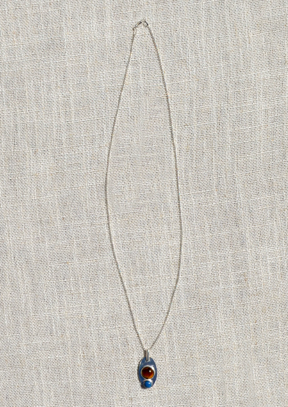 A silver necklace with pendant adorned with a brown gemstone and blue gemstone.