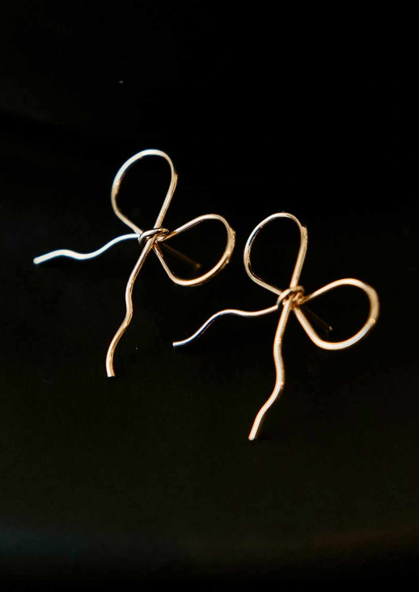 A pair of handmade earrings in bow shape made from gold wire.