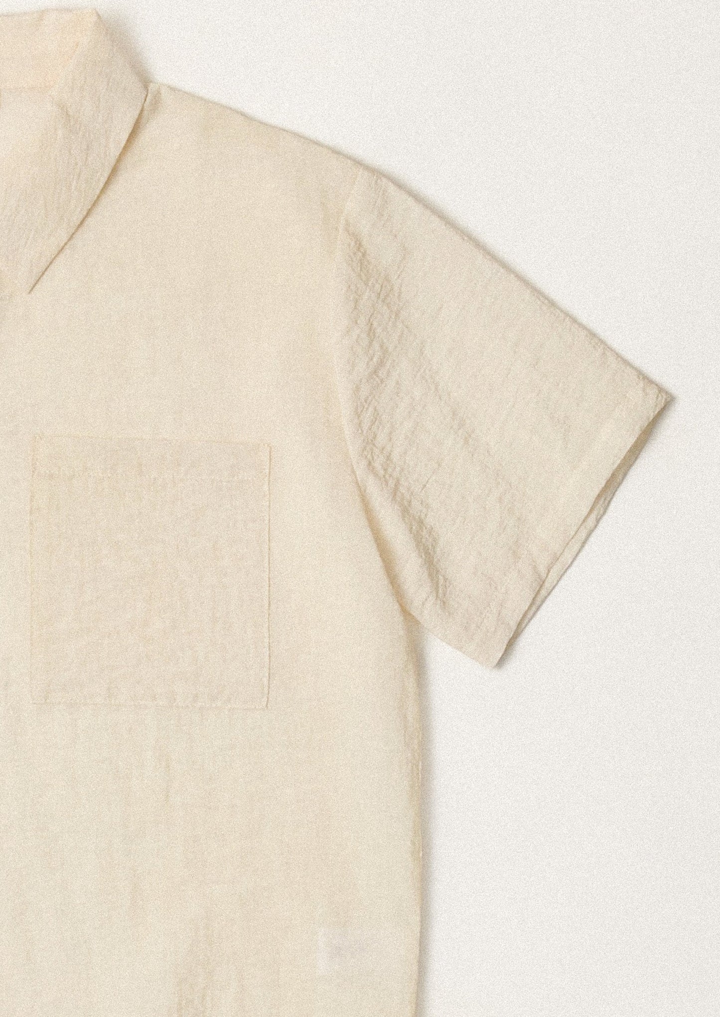 A woman wearing a short sleeve collared button front shirt in cream with soft wrinkled texture.