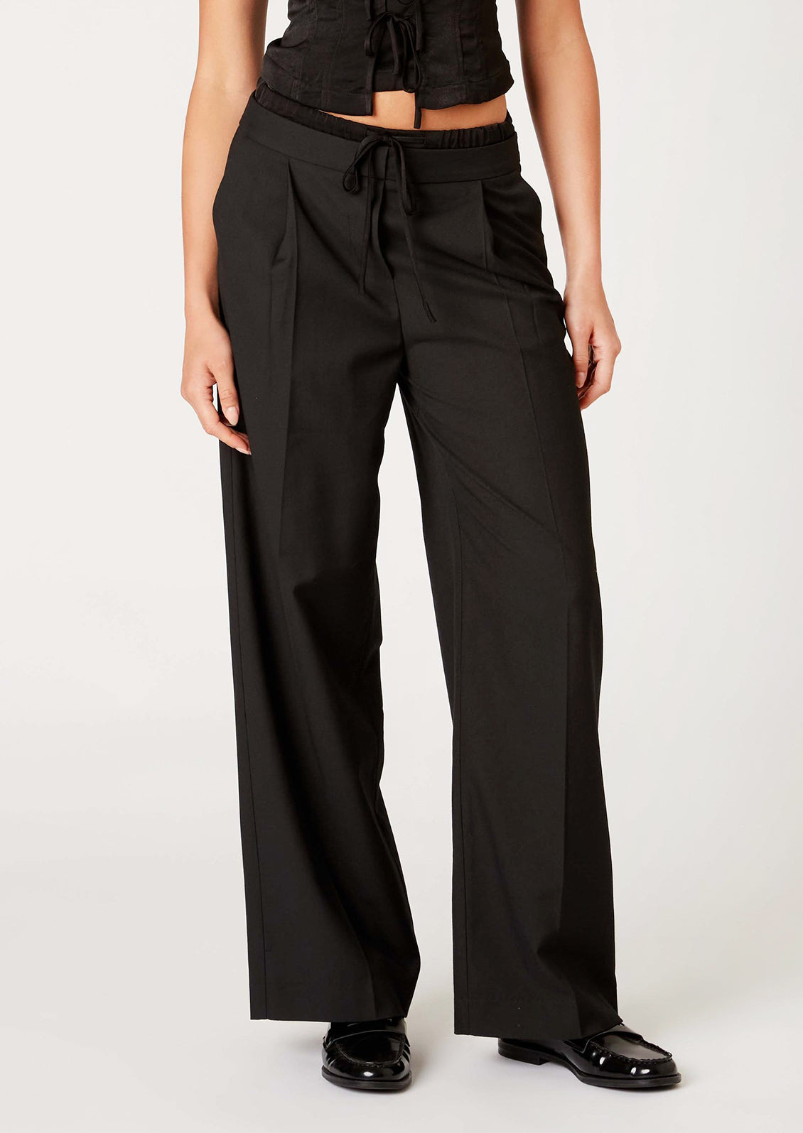 A woman wearing a pair of pants in black with ruched waistband detailing.