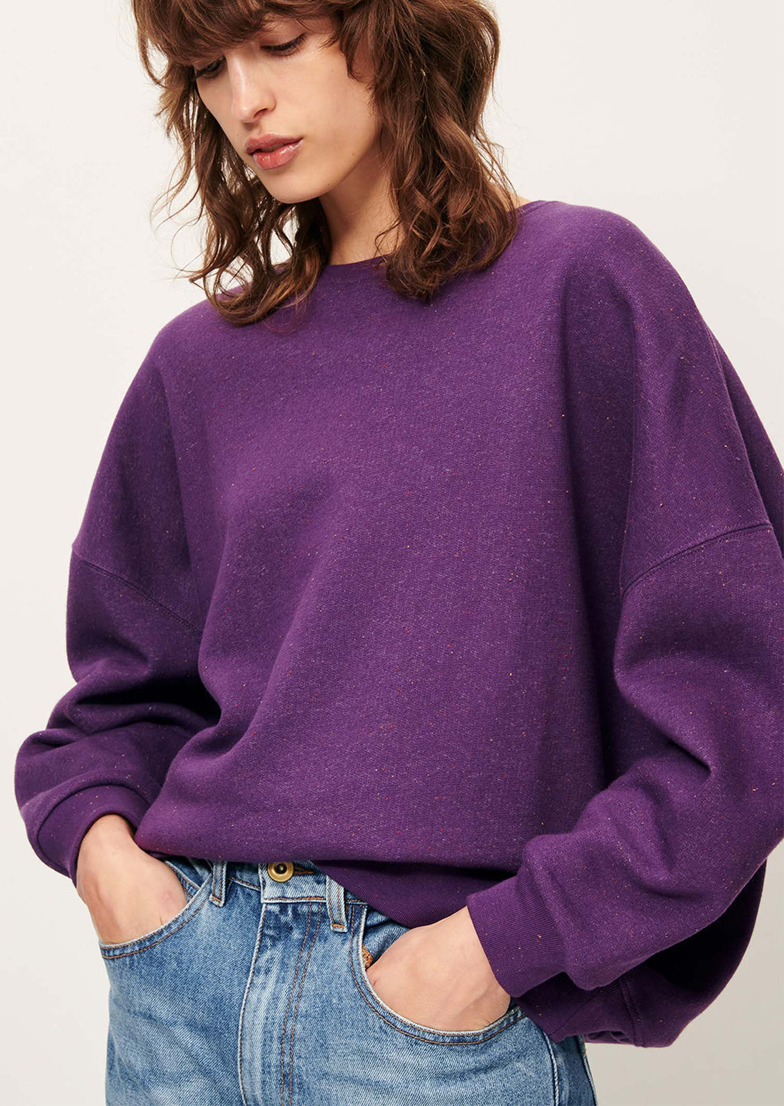A woman wearing a relaxed fit sweatshirt in vibrant purple with speckles in fabric.