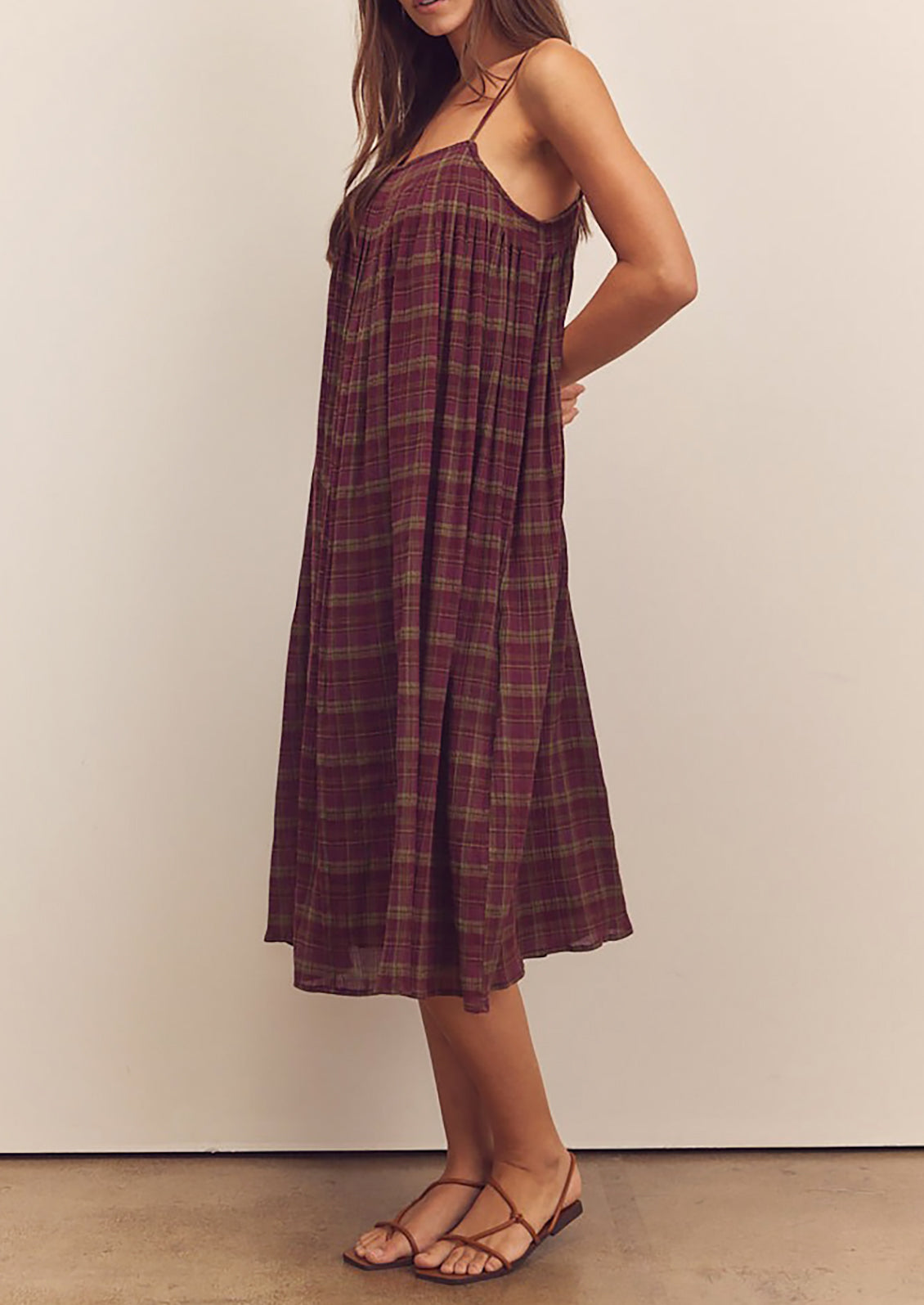 A person wearing a midi length dress in burgundy and green plaid pattern with thin straps.