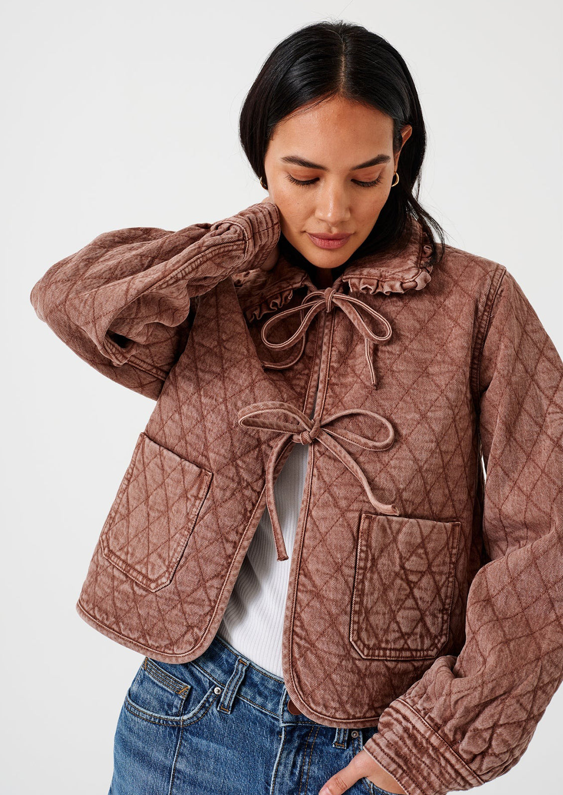 A woman wearing a mauve colored jacket with diamond quilting and bow tie front.