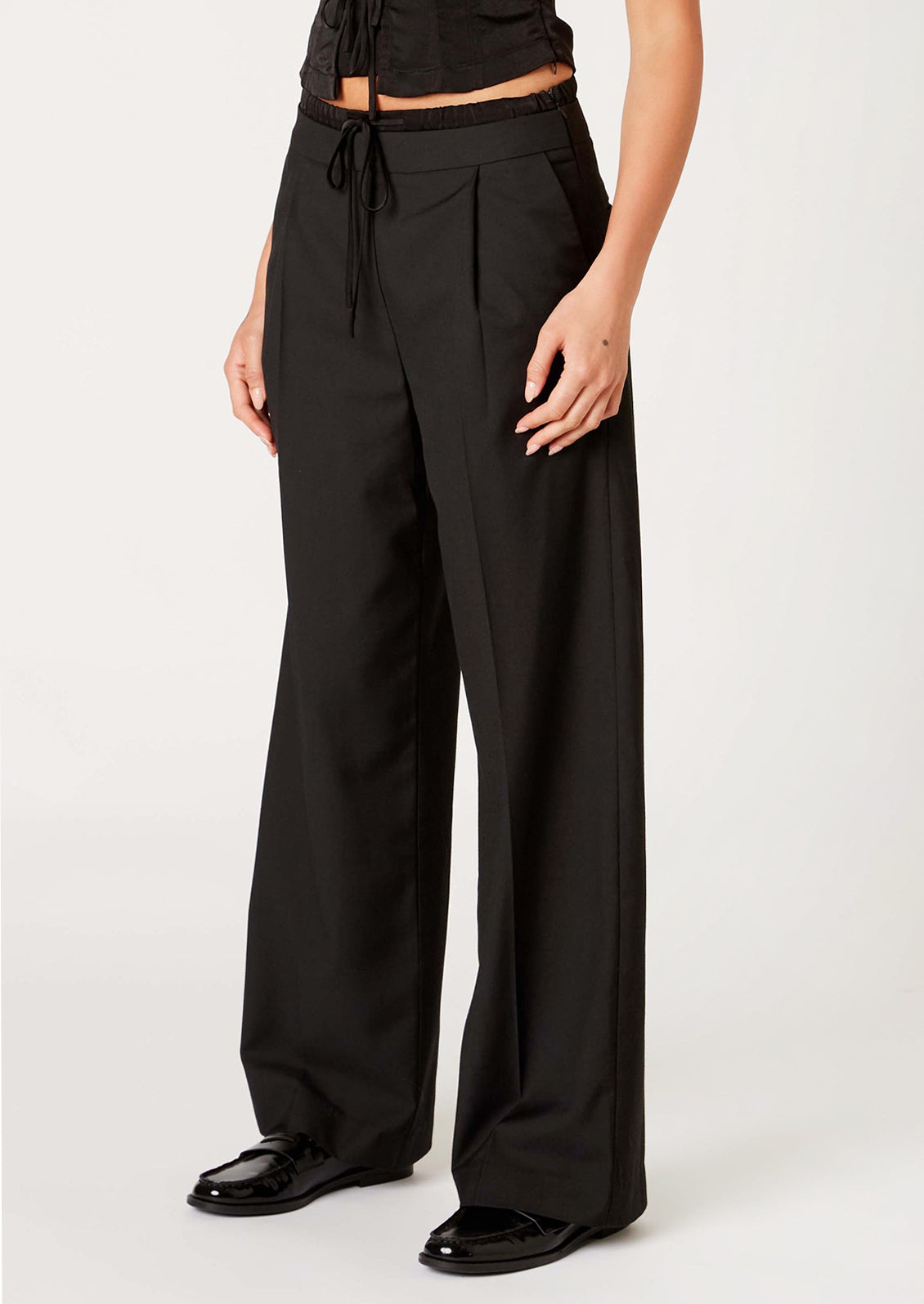 A woman wearing a pair of pants in black with ruched waistband detailing.