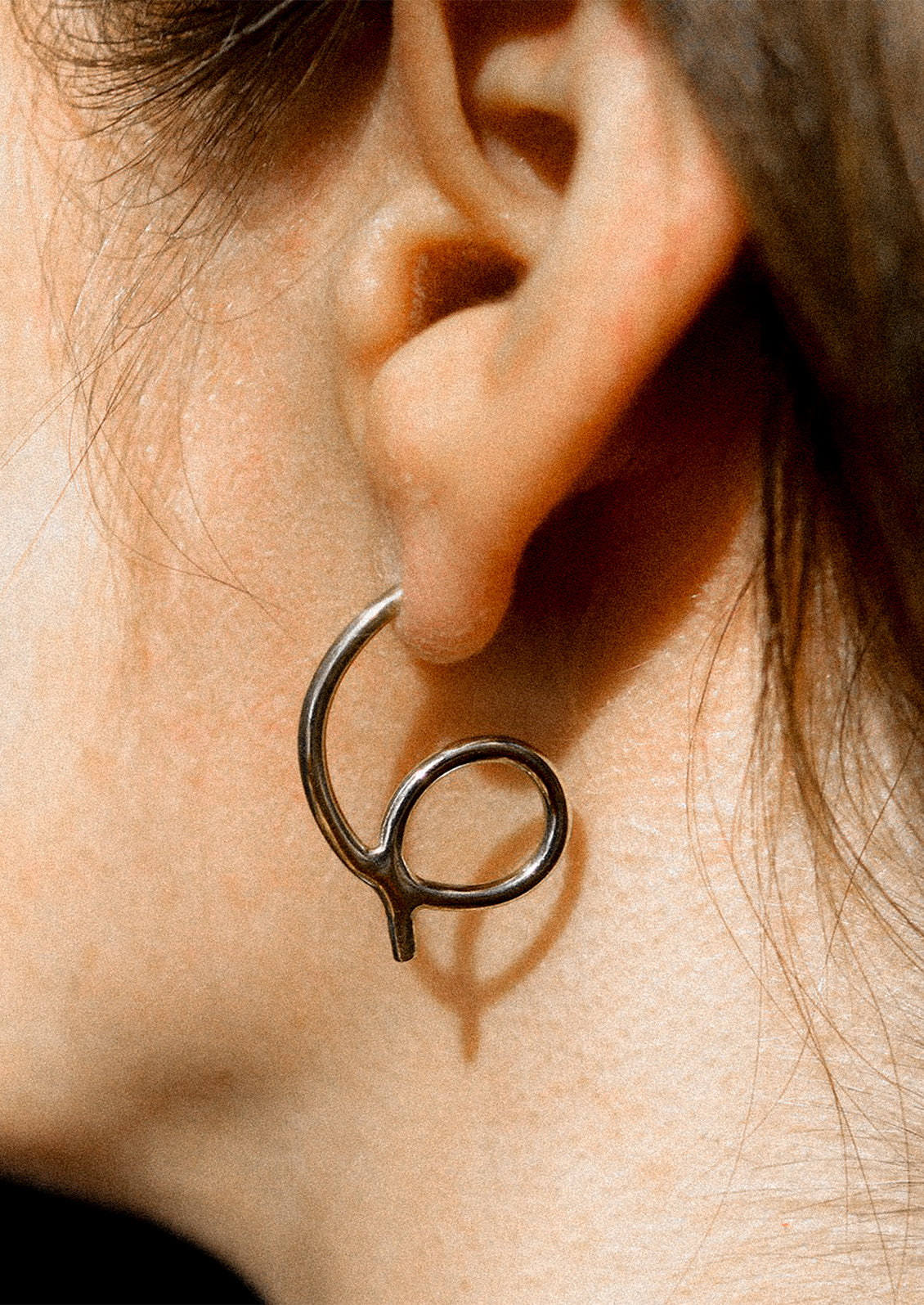 A person wearing a loop shaped sterling silver stud earring.