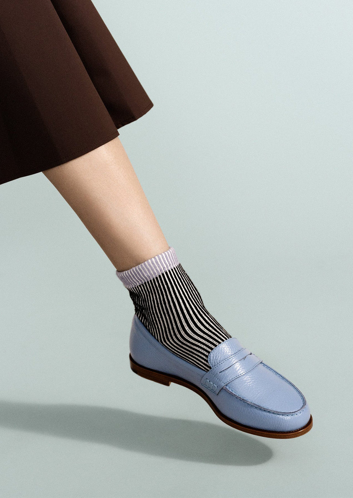 Light blue loafers worn with striped socks on a light gray background