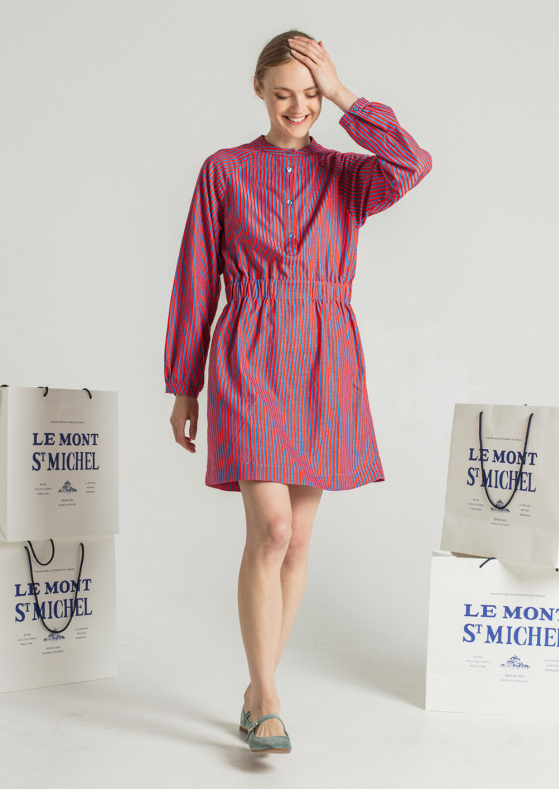 A woman wearing a long sleeved short dress in blue and red vertical stripe pattern.