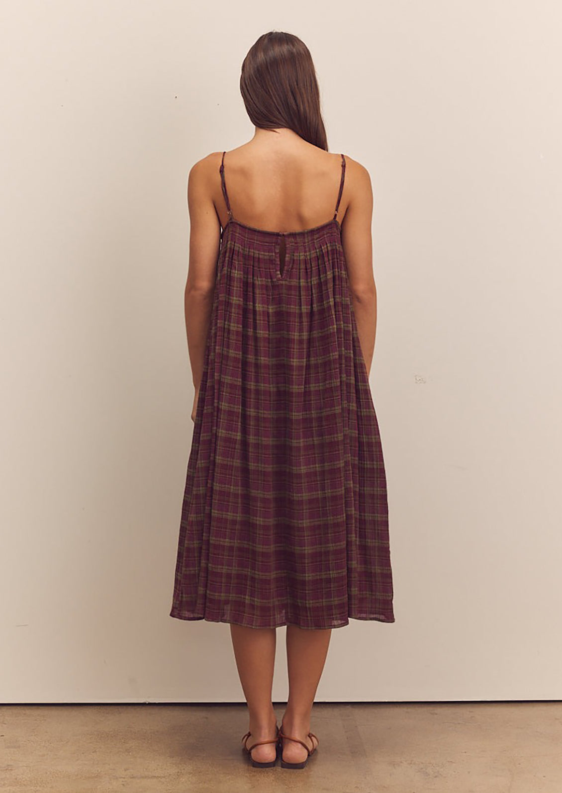 A person wearing a midi length dress in burgundy and green plaid pattern with thin straps.
