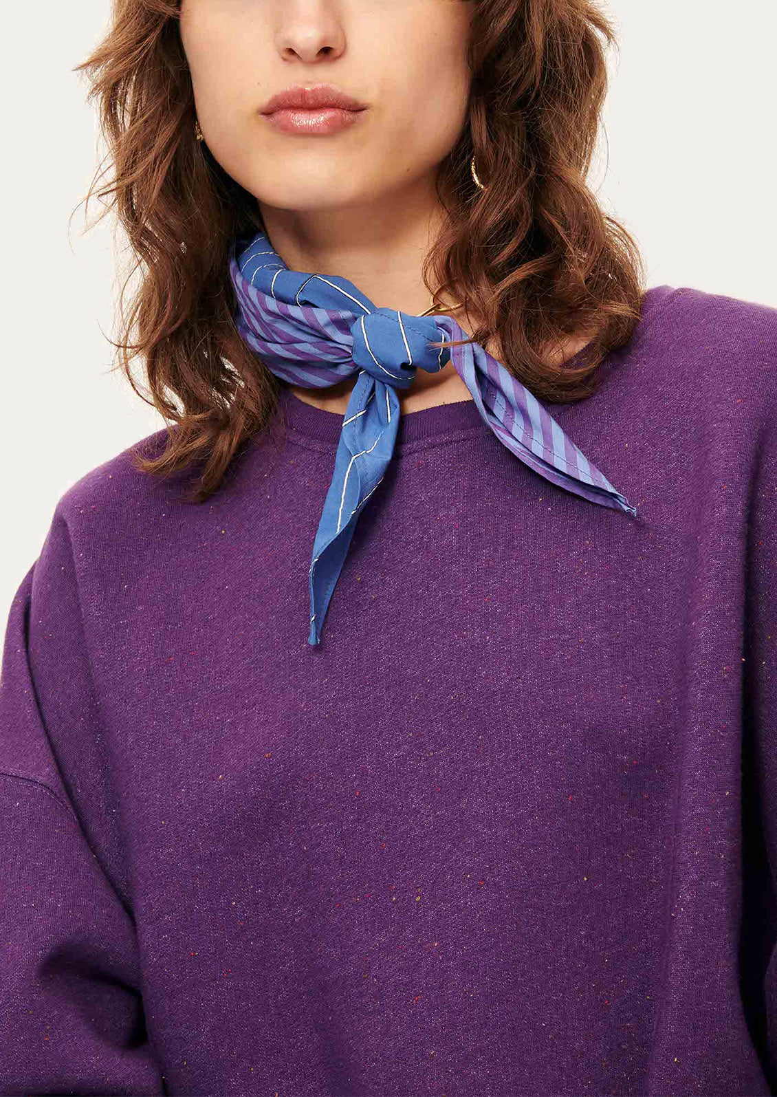 A woman wearing a relaxed fit sweatshirt in vibrant purple with speckles in fabric.