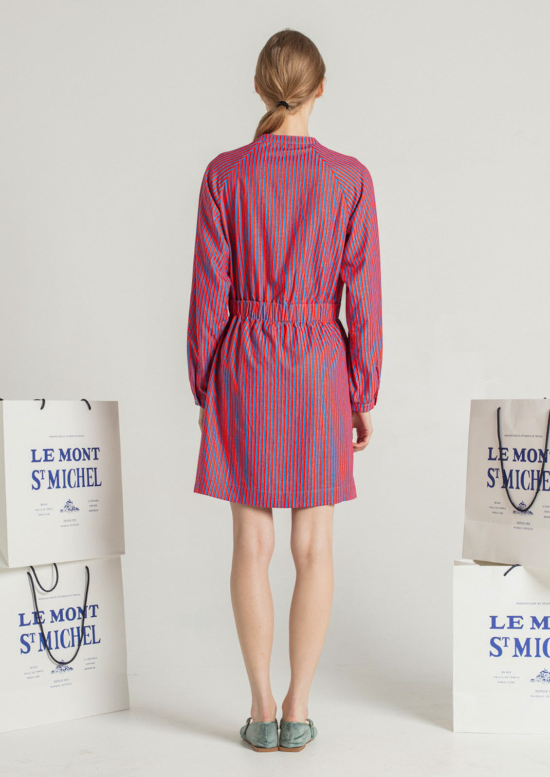 A woman wearing a long sleeved short dress in blue and red vertical stripe pattern.