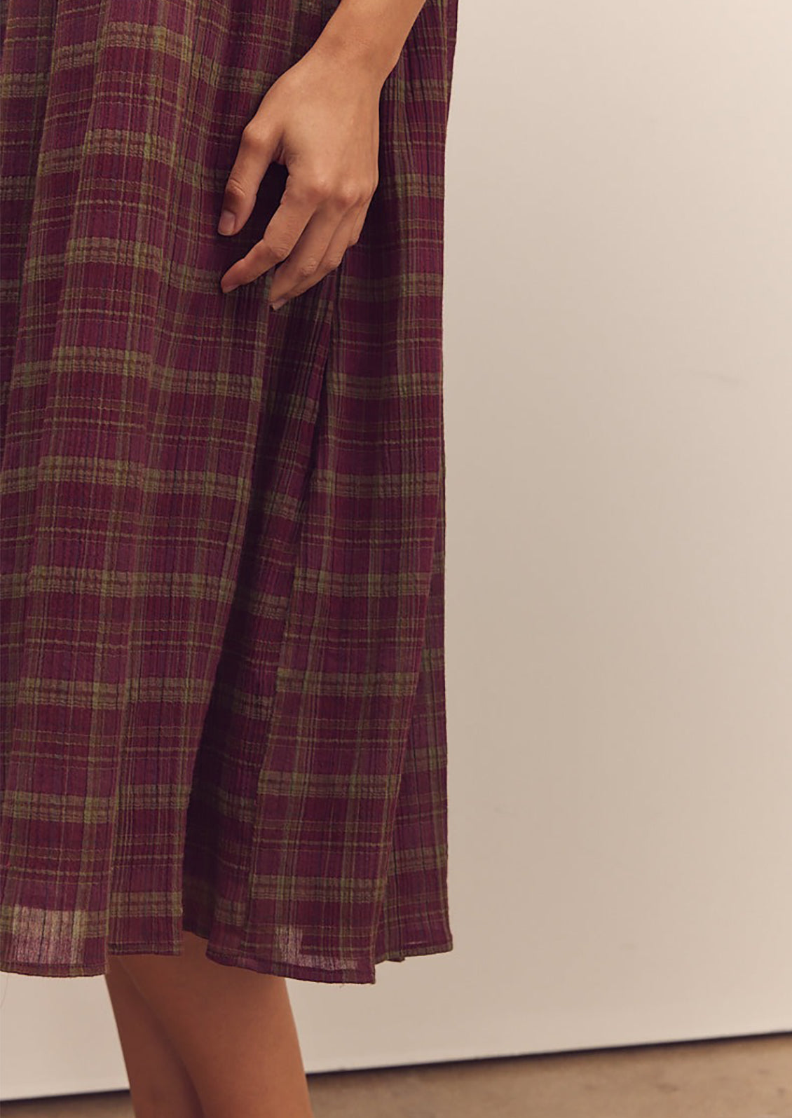 A person wearing a midi length dress in burgundy and green plaid pattern with thin straps.