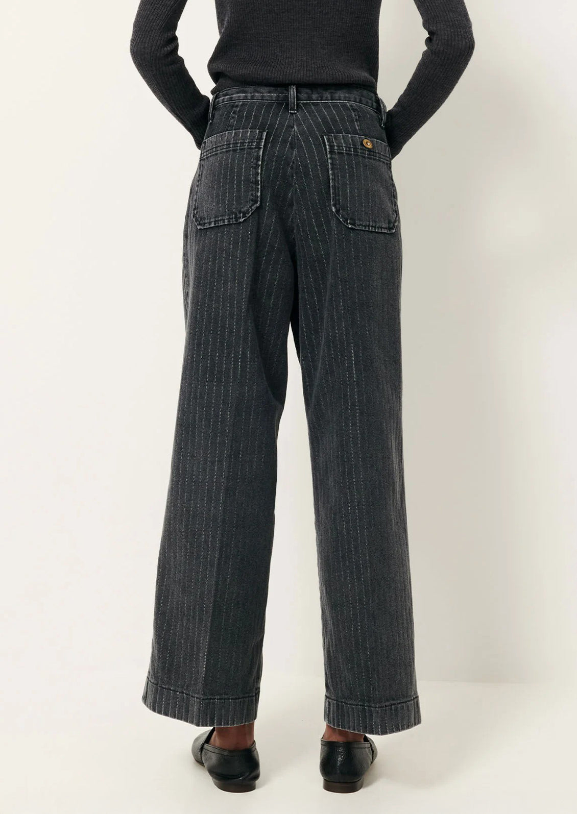 A person wearing a pair of wide leg jeans in charcoal pinstripe denim.