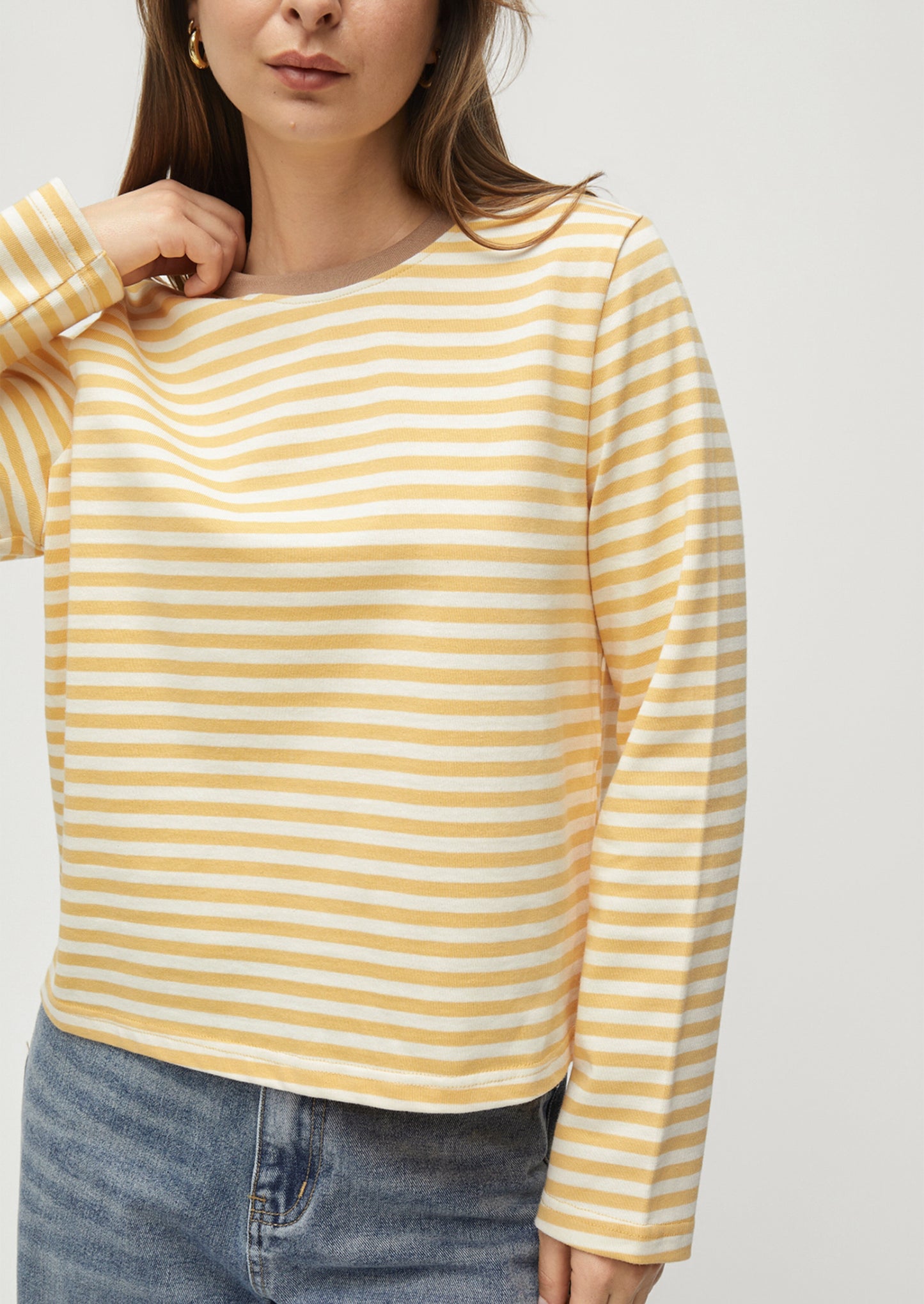 Woman wearing a yellow and white striped long-sleeve shirt with blue jeans on a light gray background