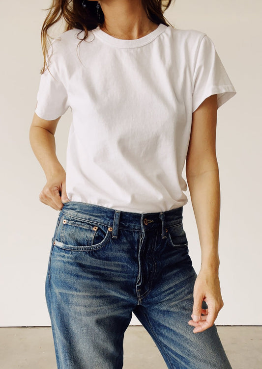 Person wearing a plain white t-shirt and blue jeans against a neutral background