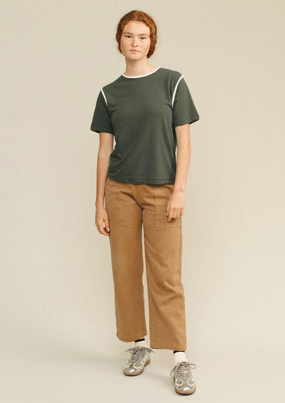 Person wearing a green t-shirt and brown pants on a beige background